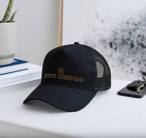 Casquette trucker noire Mutu Likolo – Collection Résilience, posée sur une table à côté d’un trousseau de clés, symbole de style et de confiance.
Black Mutu Likolo trucker cap – Resilience Collection, placed on a table next to a set of keys, symbol of style and confidence. 





